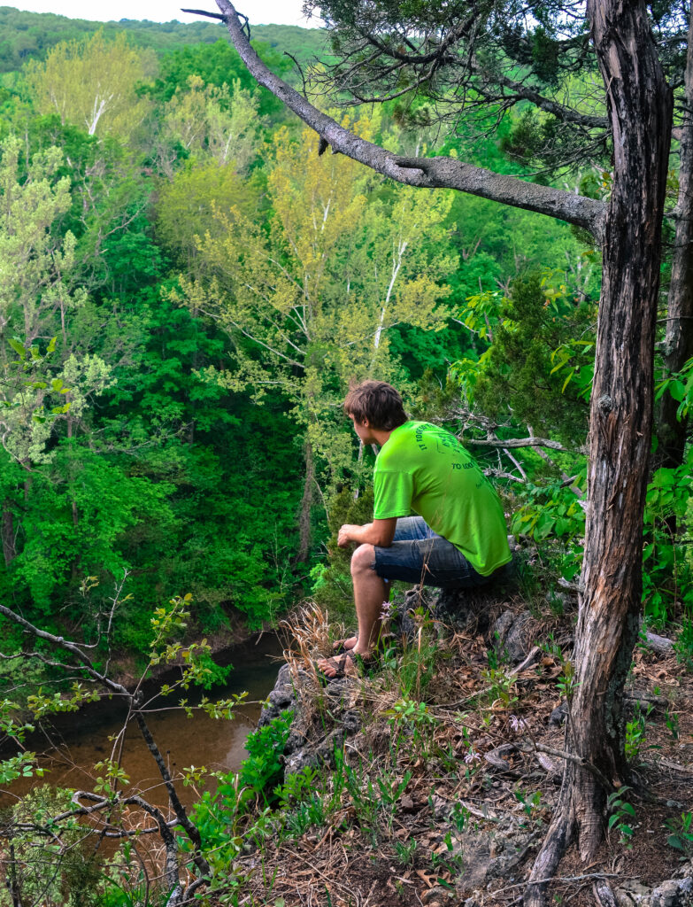 Man in a green shirt sitting on a bluff overlooking the tree-lined Meramec River