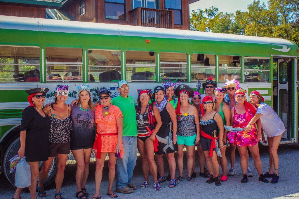 Float trip group in costume posing beside a green Ozark Outdoors shuttle bus