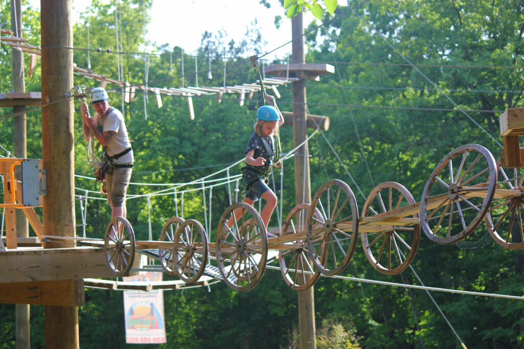 Adult and child in helmets crossing a rope and wagon-wheel bridge at Floating Treetops Aerial Park