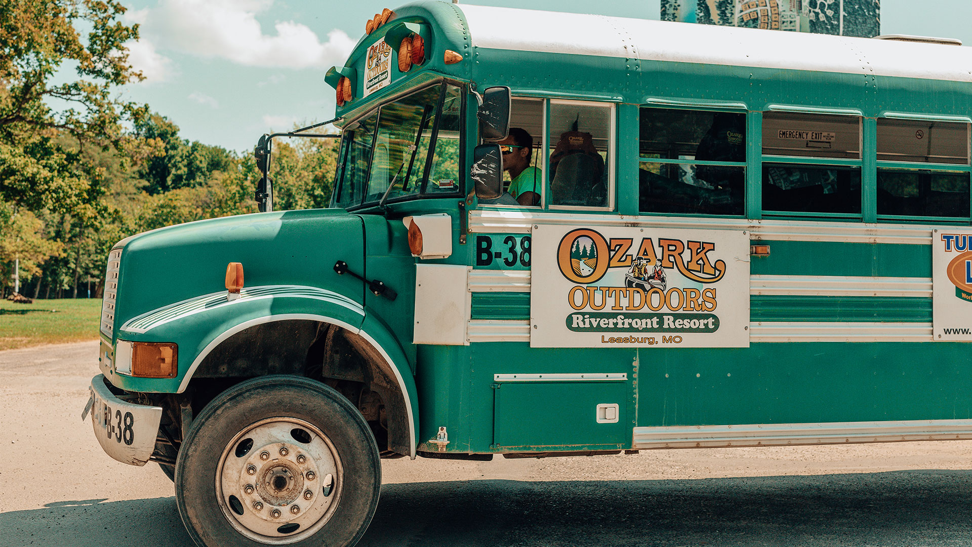 Green Ozark Outdoors shuttle bus parked with the driver aboard