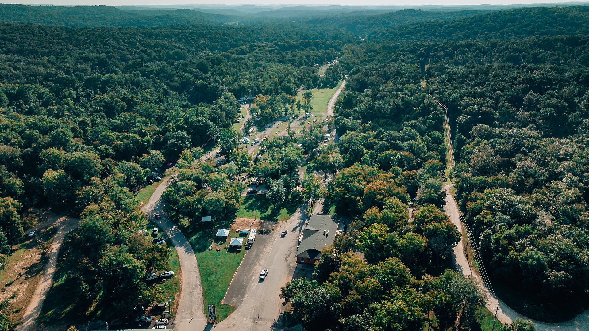 Aerial view of Ozark Outdoors Resort in a forested Ozark valley, campsites and roads winding through the trees