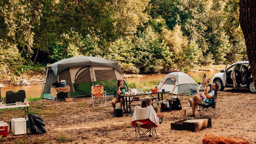 Campers gathered around a picnic table at a riverfront group campsite with tents beside the Meramec River