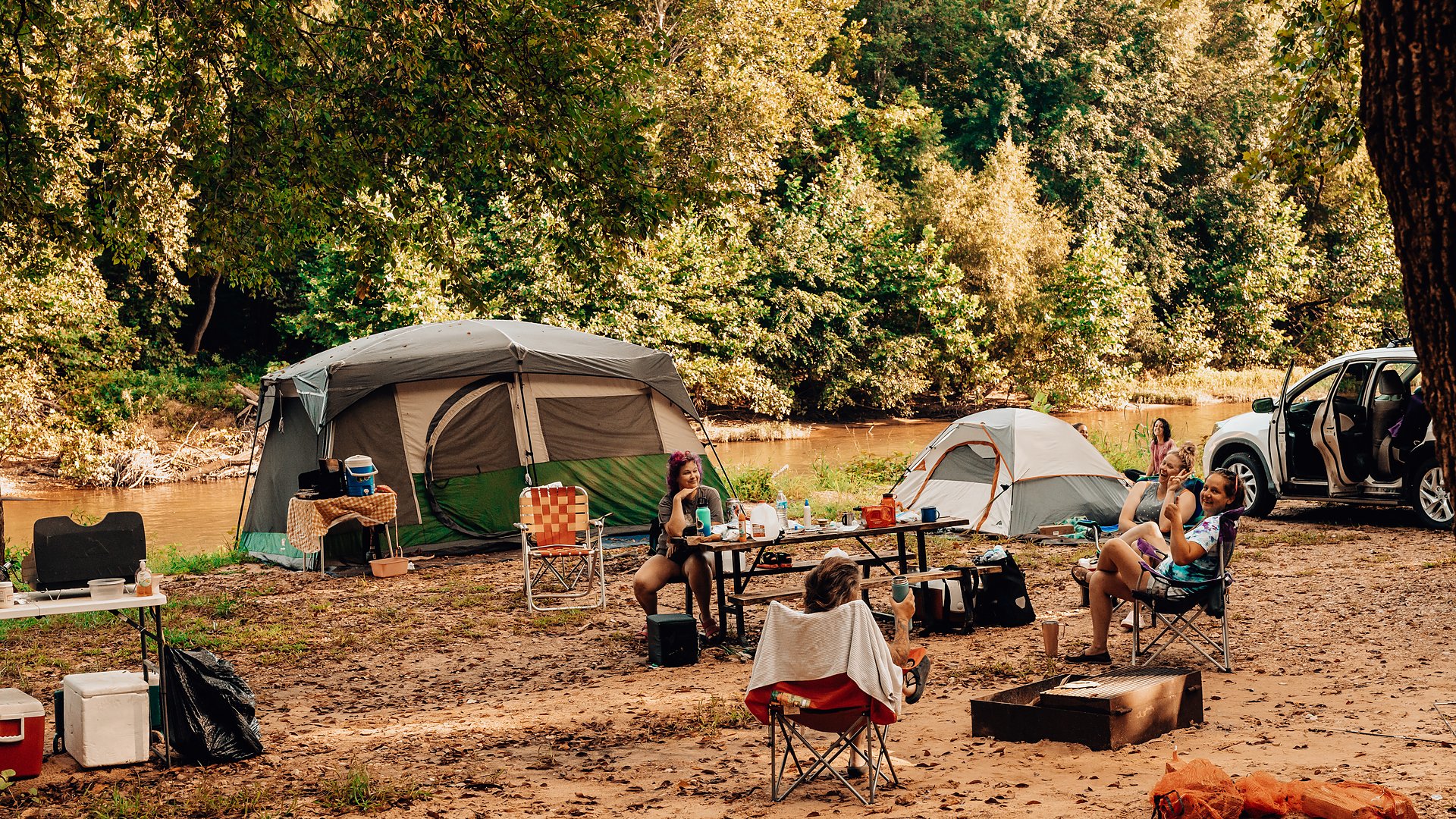 Campers gathered around a picnic table at a riverfront group campsite with tents beside the Meramec River