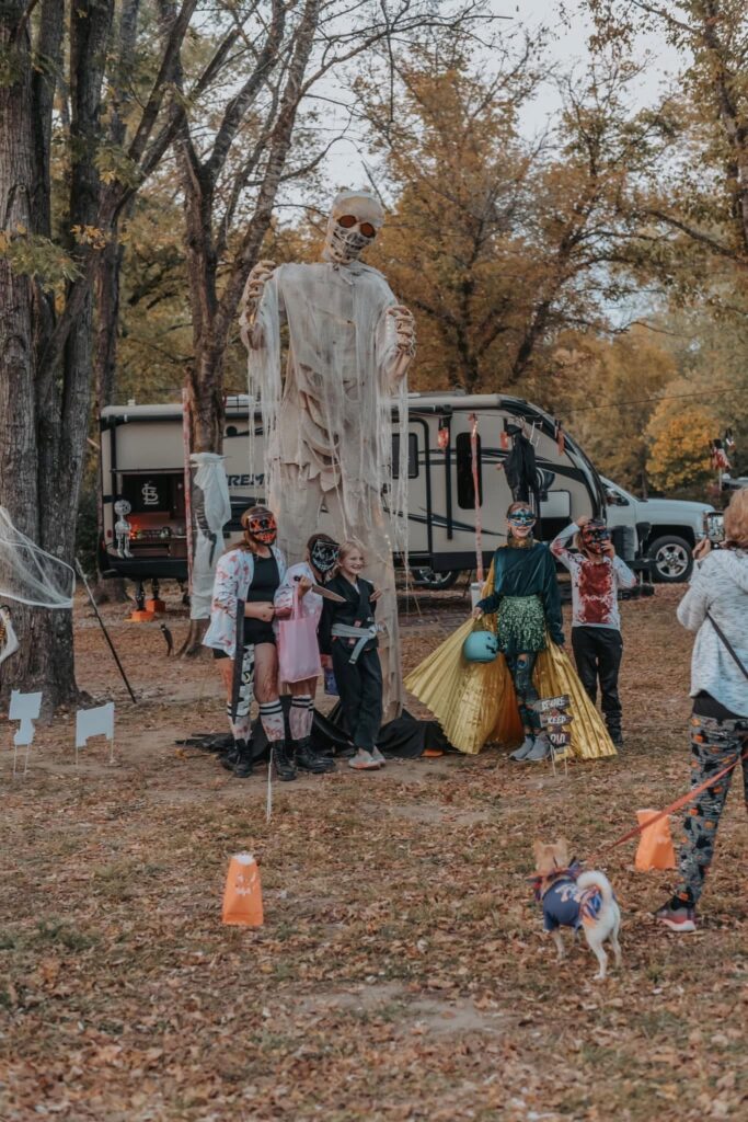 Towering ghost figure standing over a decorated RV campsite as costumed guests walk past