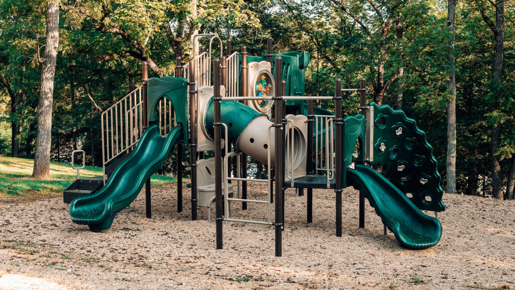 Green playground with slides and climbing structures among the trees at Ozark Outdoors Resort