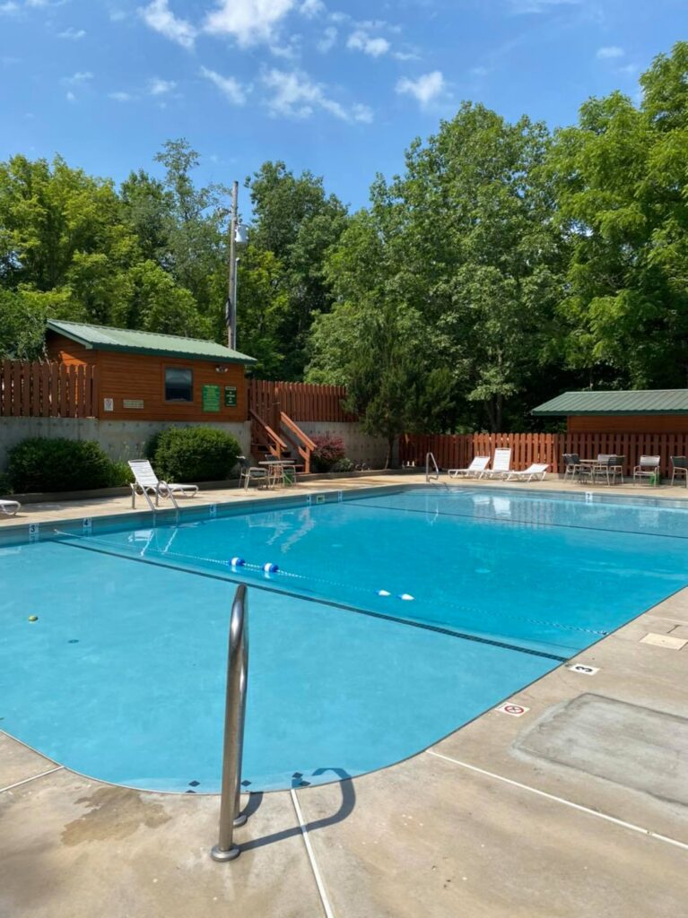 Outdoor swimming pool with lounge chairs and a log cabin behind it at Ozark Outdoors Resort